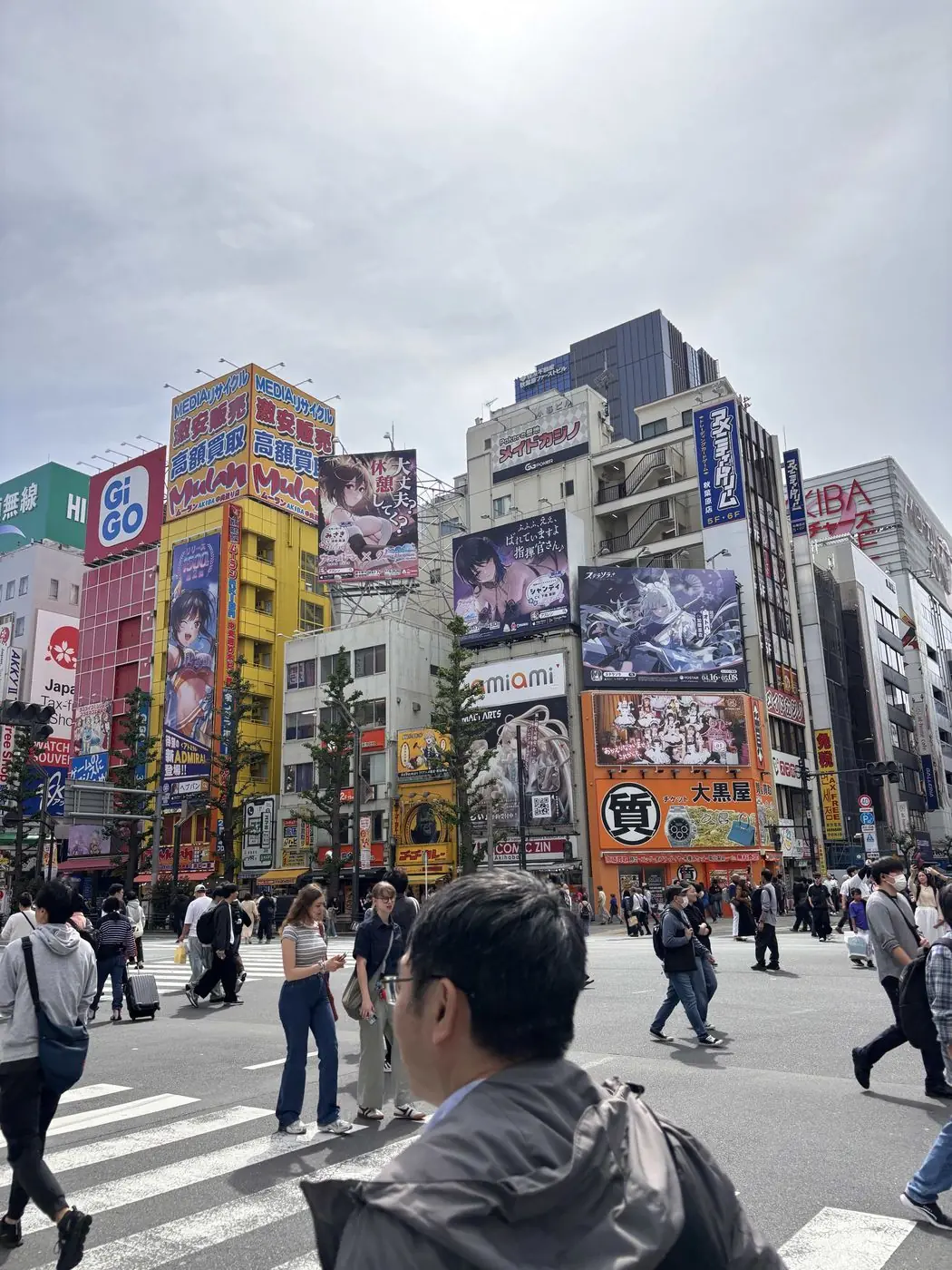 A busy Tokyo crossing framed by tall buildings covered in illustrated billboards