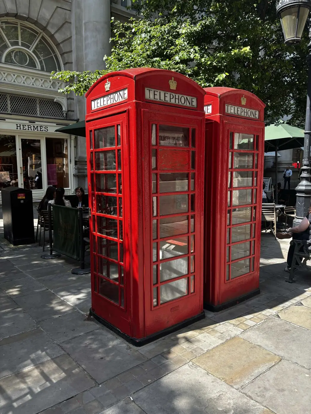 Two red telephone boxes on a paved London street